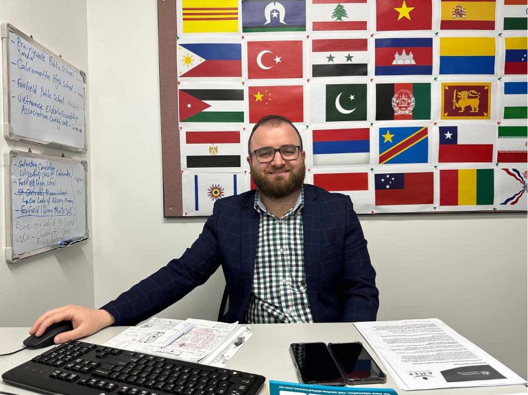 Basim Shamaon sitting at a desk with national flags in the background