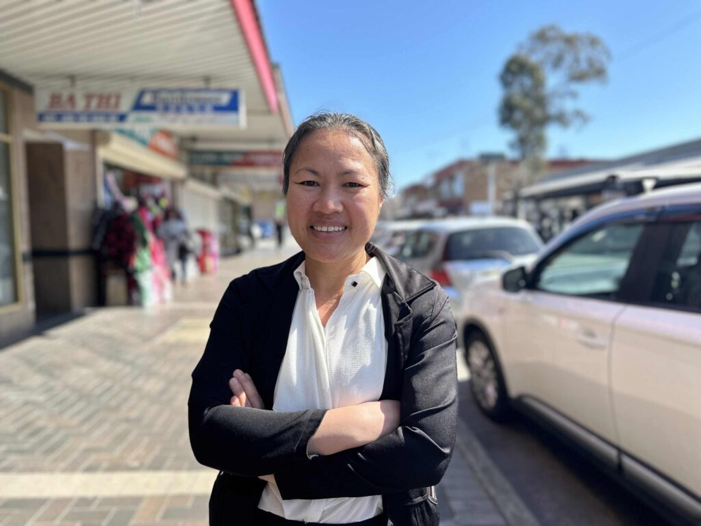 Woman wearing smart jacket and white tops stands on main street with crossed arms and a smile