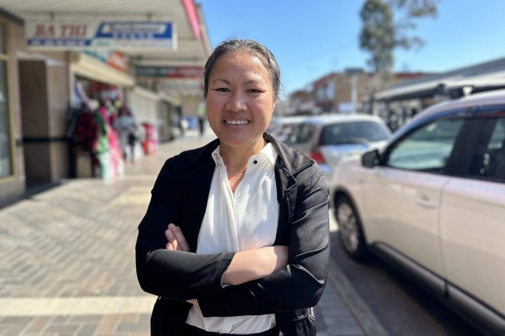 Woman wearing smart jacket and white tops stands on main street with crossed arms and a smile