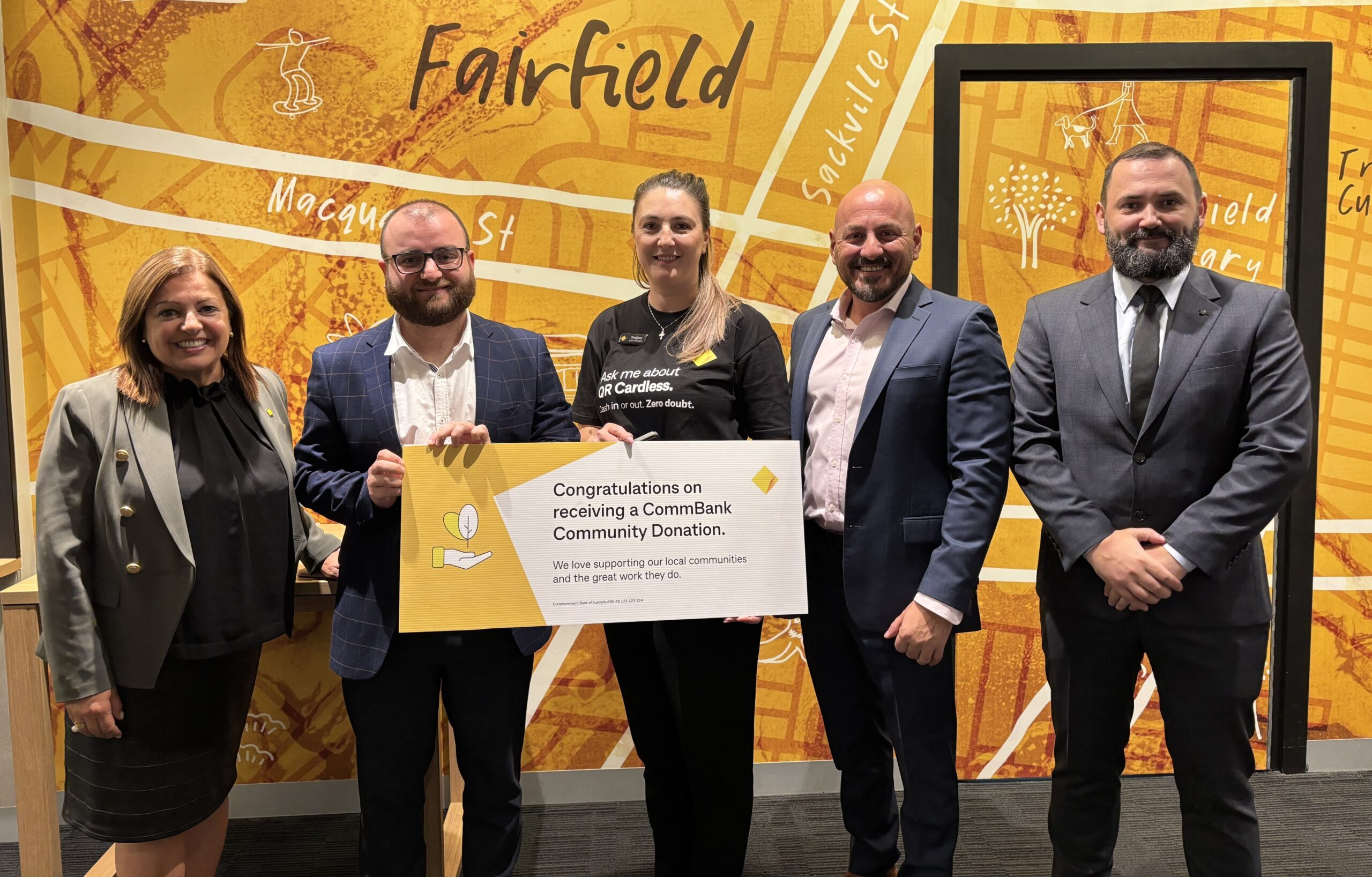 five people foru men and one woman hold a cheque for $5000 in front of wall that says Fairfield