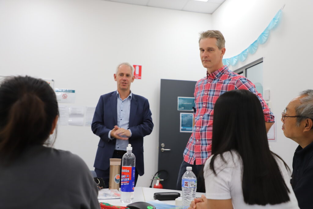 Two men in  suits pictured in classroom in conversation with students shown from behind