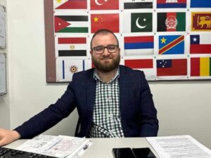 Basim Shamaon sitting at a desk with national flags in the background