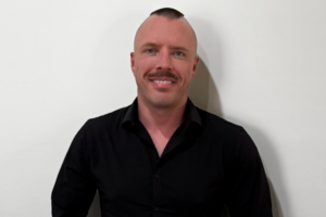 Profile photo of Alex Simpson against a white wall background - creator of the Global Voices Content Mentorship Program at NSF