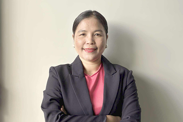 AMEP Canberra student Hnin standing in front on a beige coloured wall, wearing a suit jacket and crossing her arms 600x400