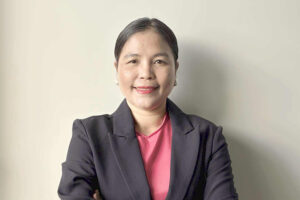AMEP Canberra student Hnin standing in front on a beige coloured wall, wearing a suit jacket and crossing her arms 732x488