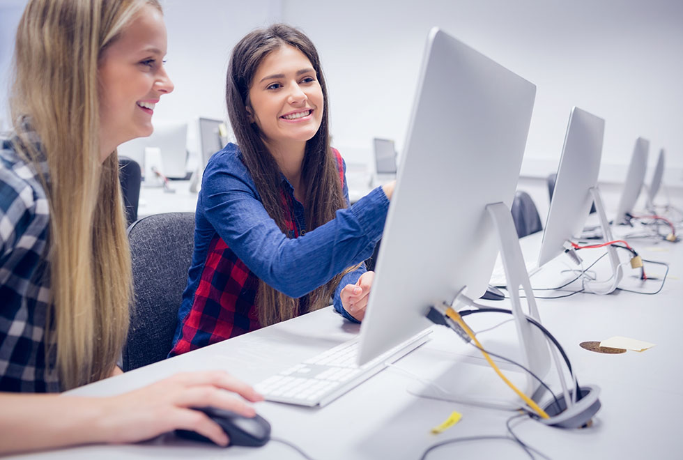 Two female NSF students sitting in a computer laboratory, with one student pointing towards a desktop monitor (980x660)