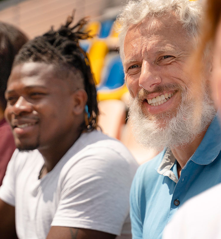 Two men sitting in the stands at a football field and smiling (740x800)