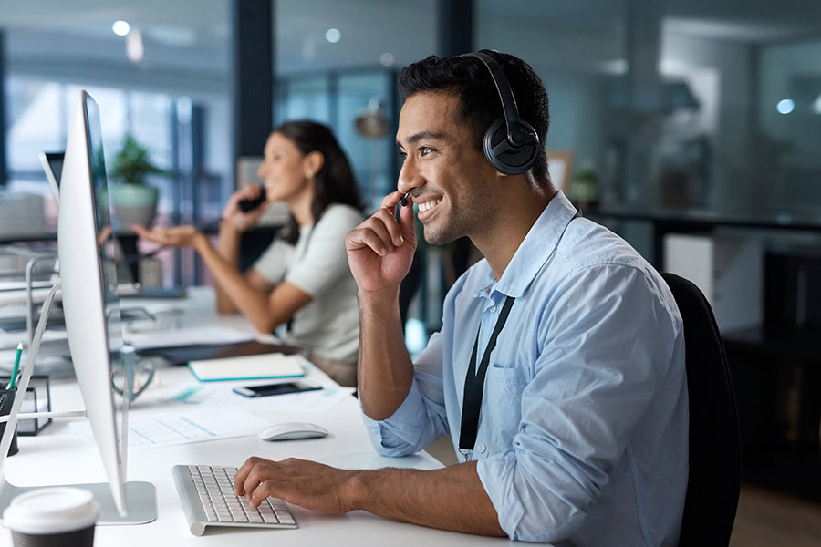 A young customer service worker sitting at a desk wearing a headset (900x600)