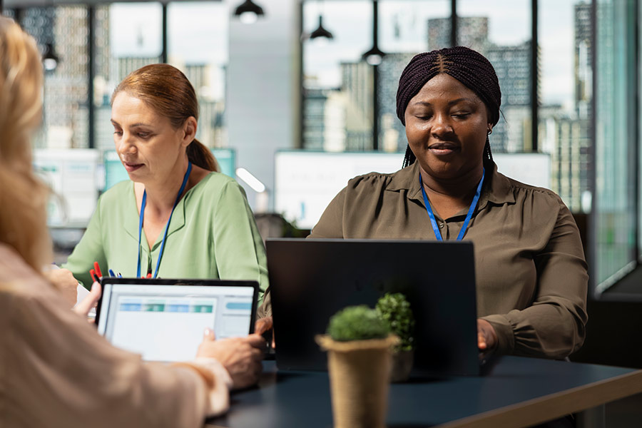 Two female employment service provider working from laptops and wearing lanyards (900x600).