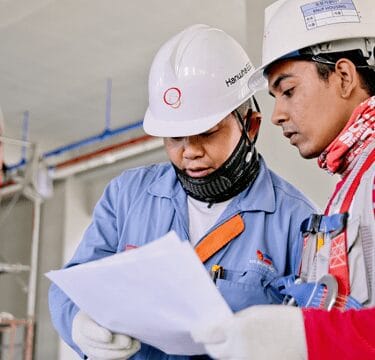 Two people wearing hard hats reviewing a document