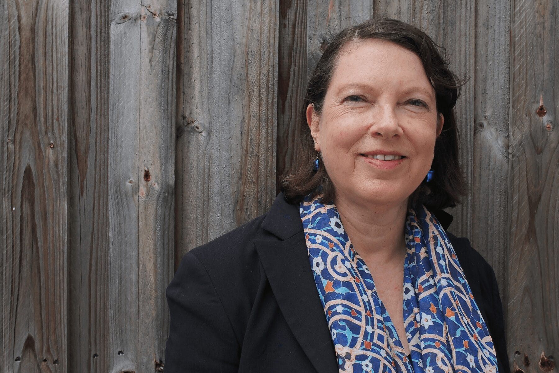 Smiling woman standing in front of wooden fence