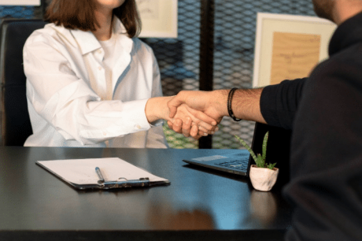 A man and woman sitting across from each other at a desk and shaking hands