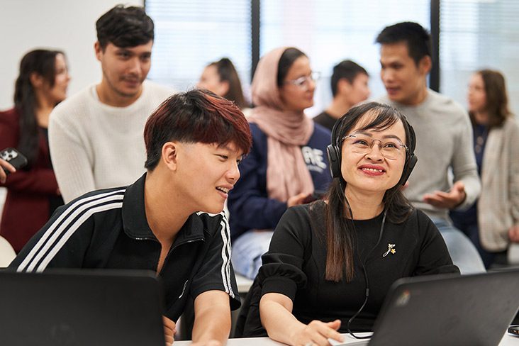 Two short course students at Navitas Skilled Futures sitting at a desk with laptops in front of them. The male student is looking towards the laptop screen in front of the female student (732x488)