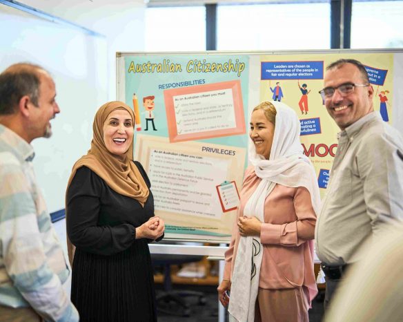Four students standing in front of a noticeboard reading Australian citizenship key facts in a classroom