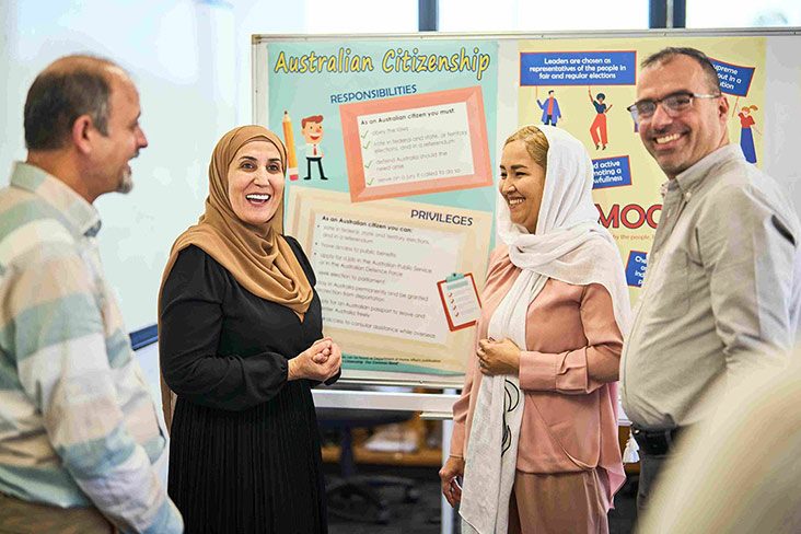 Several students standing in a classroom together in front of a whiteboard (732x488).
