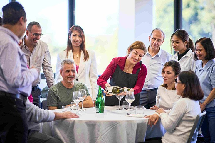 Several students from the Pathways to Work (PtW) Retail & Hospitality course sitting at a round table, with one student pouring wine into a wine glass (732x488).